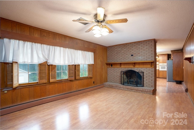 unfurnished living room featuring ceiling fan, wood walls, a brick fireplace, baseboard heating, and light wood-type flooring