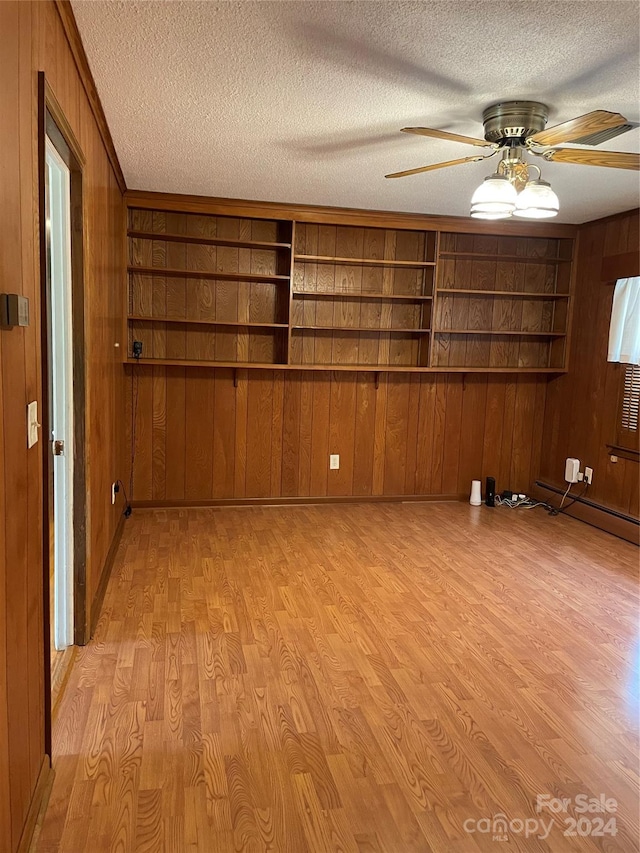 unfurnished room featuring built in shelves, a textured ceiling, wood walls, and light hardwood / wood-style floors