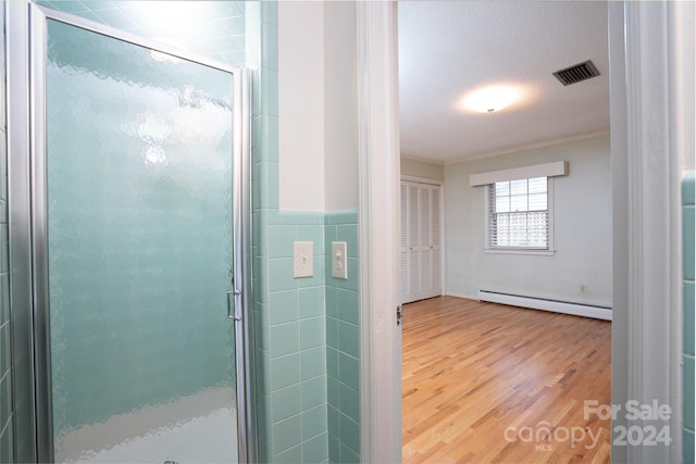 bathroom featuring tile walls, baseboard heating, hardwood / wood-style floors, and a shower with door