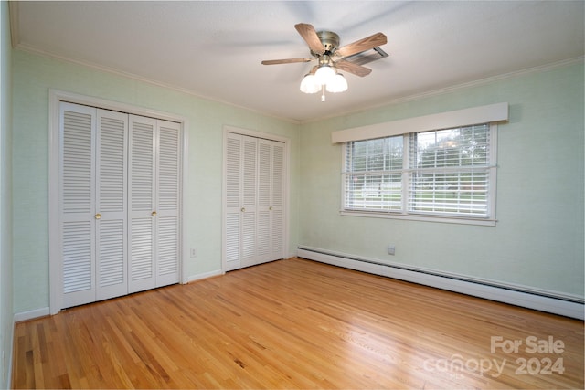 unfurnished bedroom with light wood-type flooring, ceiling fan, multiple closets, ornamental molding, and baseboard heating