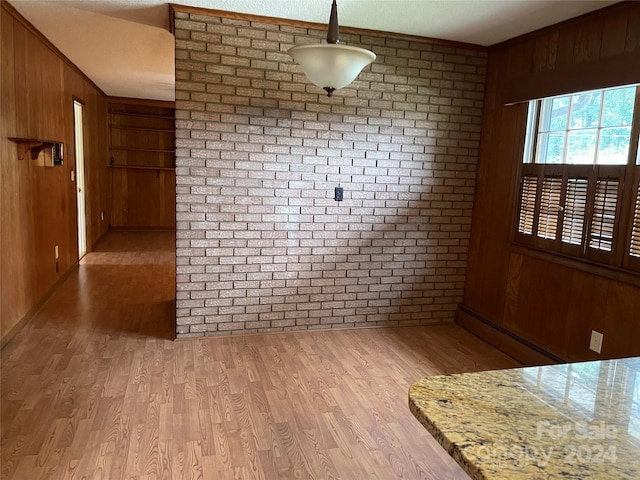 unfurnished dining area featuring light wood-type flooring, wooden walls, a baseboard radiator, and brick wall