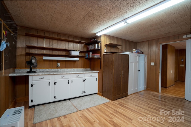 kitchen with white cabinets, wooden walls, and light hardwood / wood-style flooring