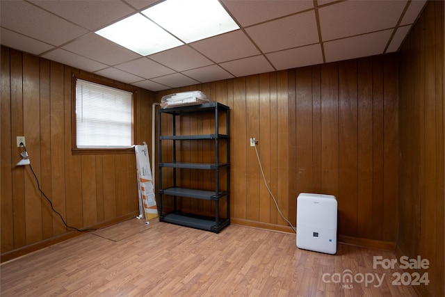 basement with a drop ceiling, light hardwood / wood-style flooring, and wooden walls