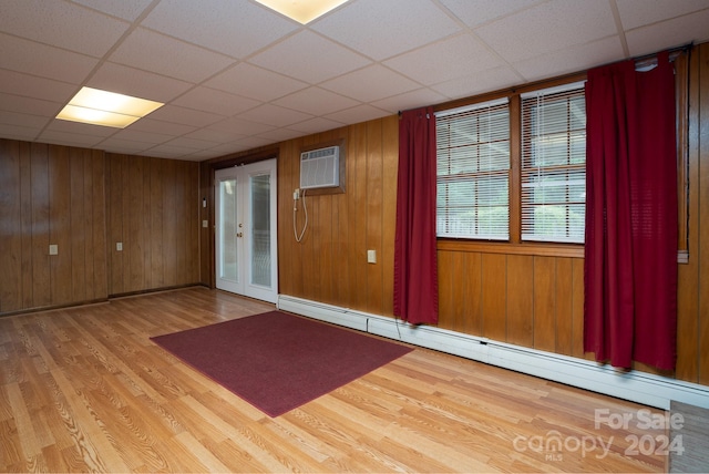 unfurnished room with a wall mounted air conditioner, wooden walls, light wood-type flooring, and baseboard heating