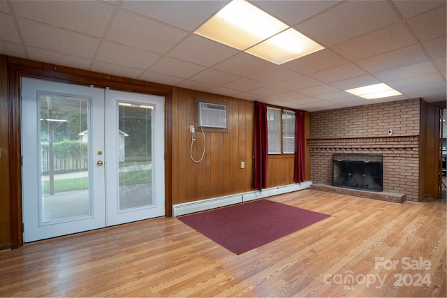 unfurnished living room with light wood-type flooring, a brick fireplace, french doors, a drop ceiling, and a baseboard heating unit