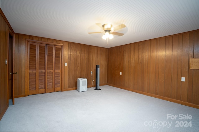 interior space with ceiling fan, light colored carpet, and wooden walls