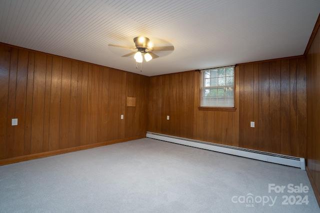 empty room featuring ceiling fan, wooden walls, and a baseboard heating unit