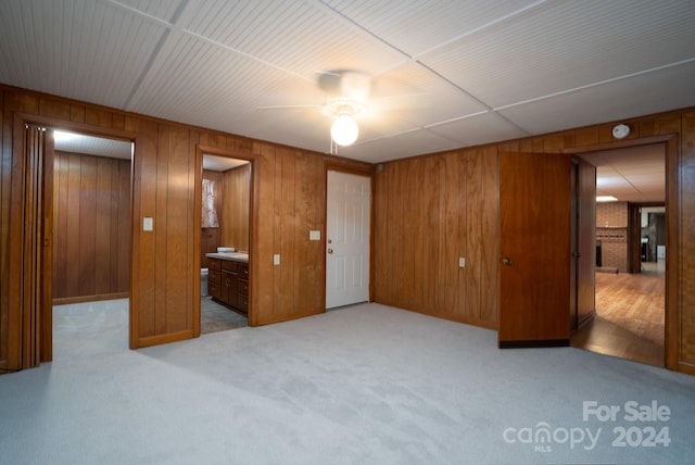 unfurnished bedroom with wood walls, ceiling fan, connected bathroom, and light carpet