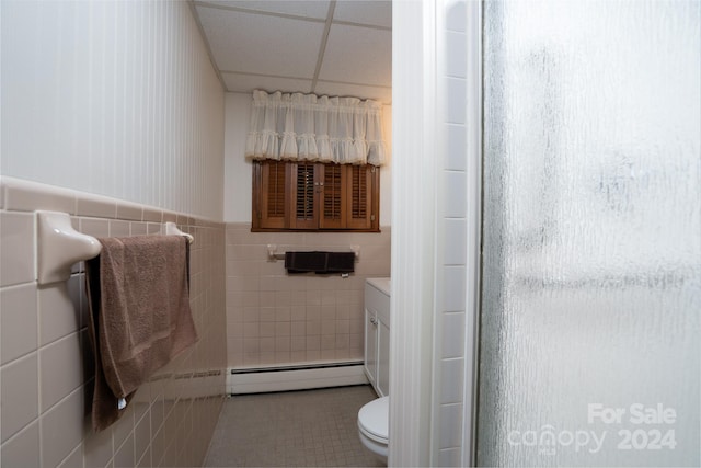 bathroom featuring vanity, a drop ceiling, tile walls, a baseboard radiator, and toilet