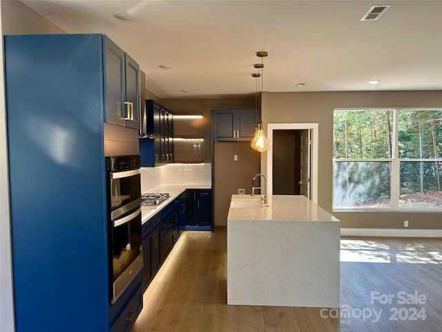 kitchen featuring pendant lighting, stainless steel appliances, a kitchen island with sink, and dark wood-type flooring