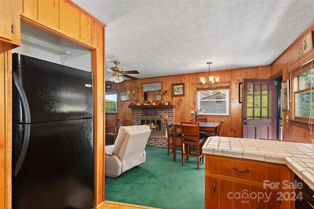 kitchen featuring light carpet, black fridge, tile counters, a fireplace, and hanging light fixtures