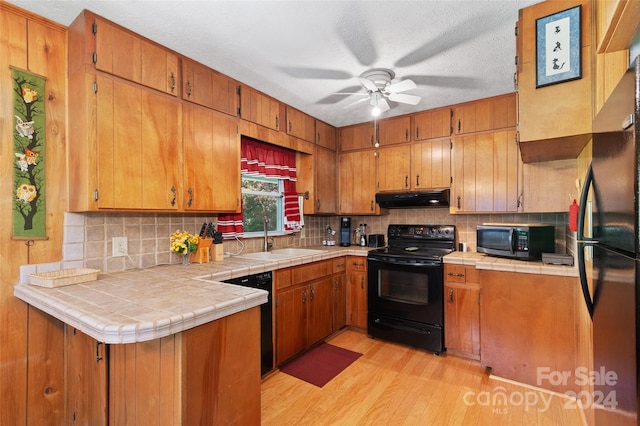 kitchen with light wood-type flooring, ceiling fan, sink, tile countertops, and black appliances