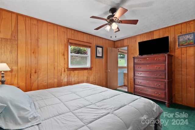 carpeted bedroom featuring wooden walls, ceiling fan, and a textured ceiling