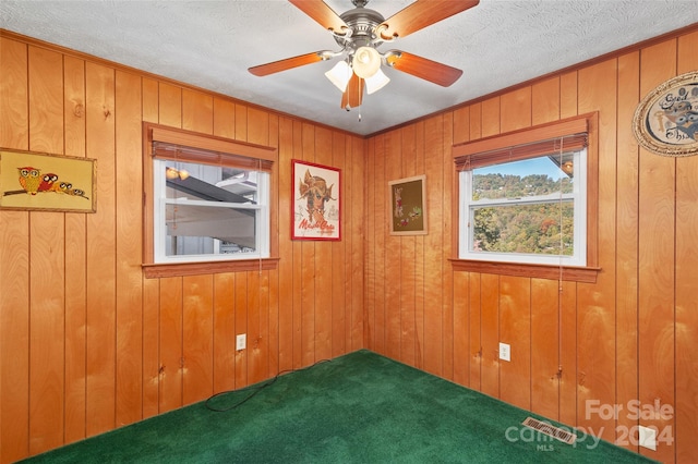 unfurnished room with ceiling fan, a textured ceiling, wooden walls, and carpet