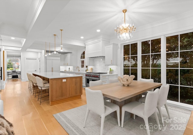 dining area featuring beamed ceiling, sink, ornamental molding, light hardwood / wood-style floors, and an inviting chandelier