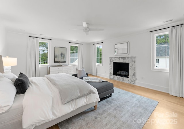 bedroom with multiple windows, a high end fireplace, light hardwood / wood-style floors, and ceiling fan