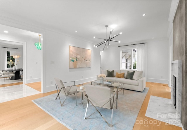 living room featuring an inviting chandelier, light hardwood / wood-style flooring, ornamental molding, and a large fireplace