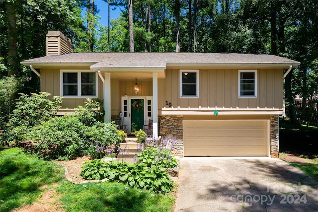 bi-level home featuring a chimney, an attached garage, stone siding, asphalt driveway, and board and batten siding