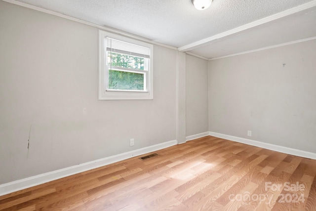 empty room featuring a textured ceiling, light wood-type flooring, and ornamental molding