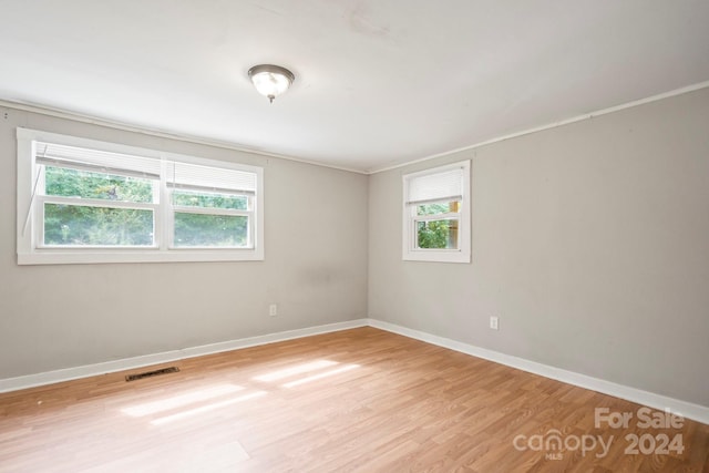 empty room featuring crown molding, light hardwood / wood-style floors, and a wealth of natural light