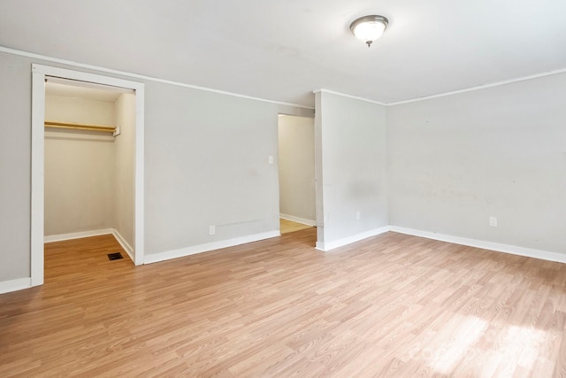 unfurnished bedroom with a closet, crown molding, light hardwood / wood-style floors, and a walk in closet