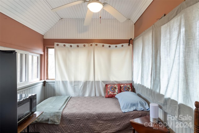 bedroom with ceiling fan, wooden walls, and lofted ceiling