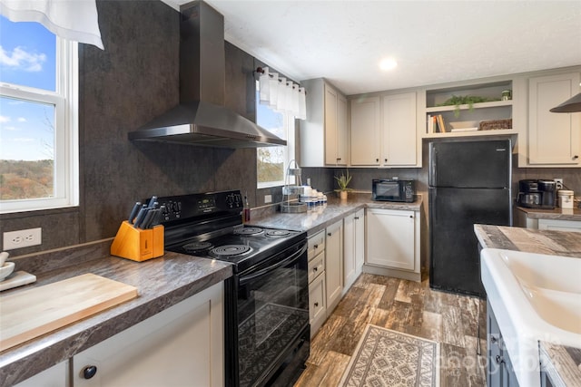 kitchen with wall chimney range hood, a healthy amount of sunlight, black appliances, and dark hardwood / wood-style flooring