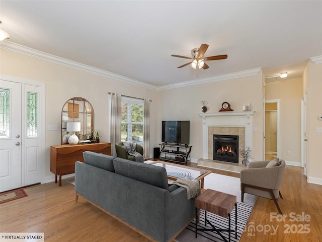 living area with a fireplace, a ceiling fan, baseboards, light wood finished floors, and crown molding