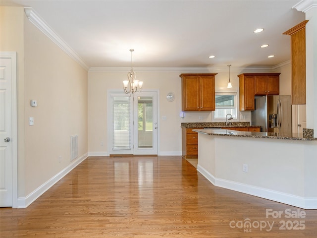 kitchen featuring decorative light fixtures, visible vents, light wood-style flooring, brown cabinetry, and stainless steel fridge