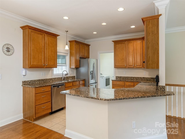 kitchen featuring appliances with stainless steel finishes, brown cabinetry, a sink, and a peninsula