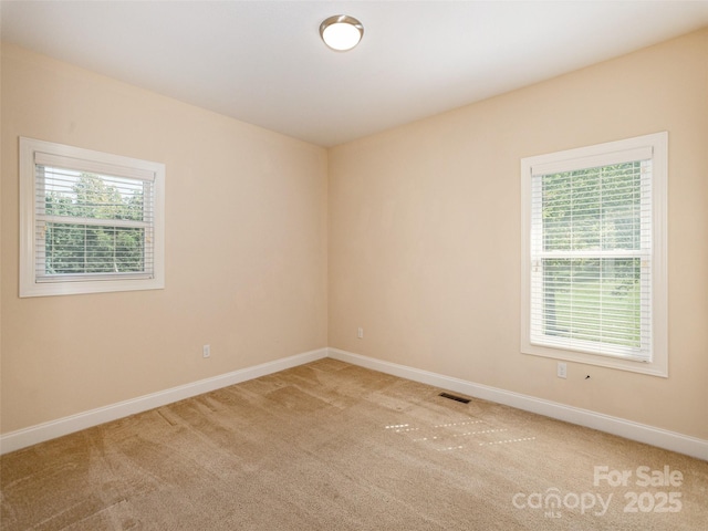 carpeted empty room featuring a wealth of natural light, visible vents, and baseboards