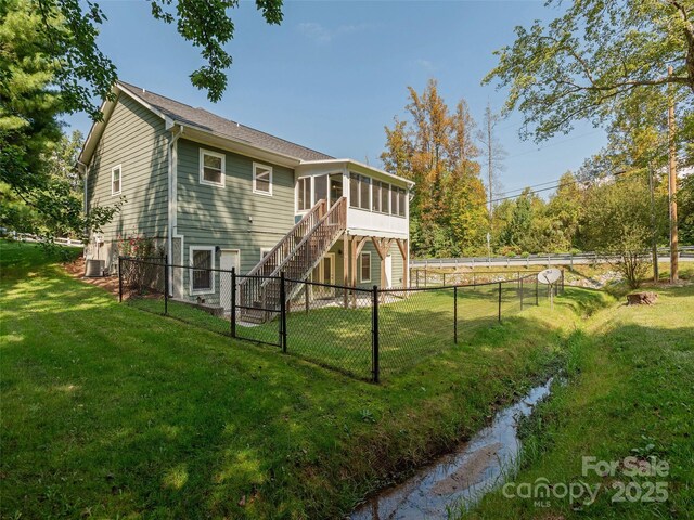 rear view of property with central AC unit, a fenced backyard, a sunroom, stairs, and a lawn