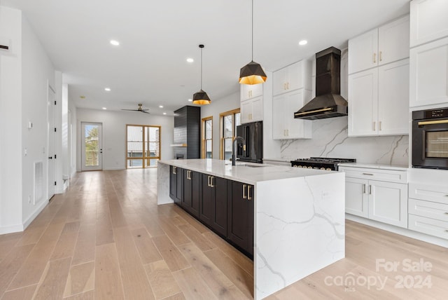 kitchen featuring black appliances, white cabinetry, wall chimney range hood, and a kitchen island with sink