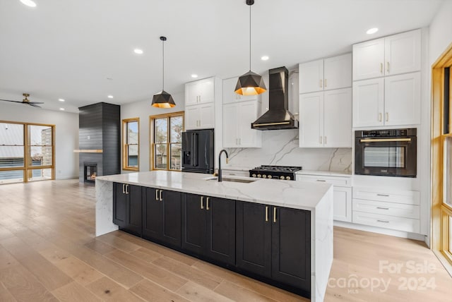 kitchen featuring a large island, sink, wall chimney exhaust hood, refrigerator with ice dispenser, and black oven