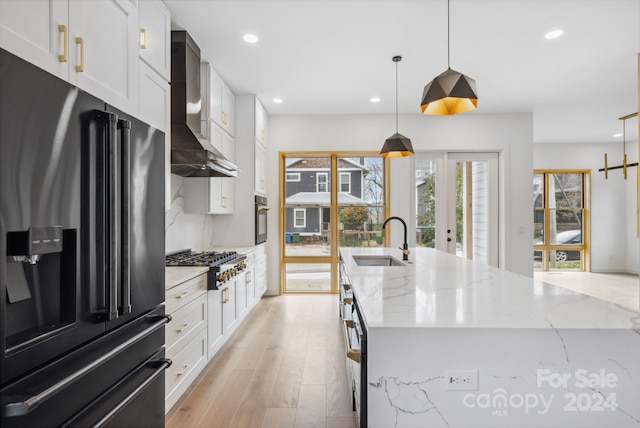 kitchen with a kitchen island with sink, hanging light fixtures, sink, wall chimney exhaust hood, and appliances with stainless steel finishes