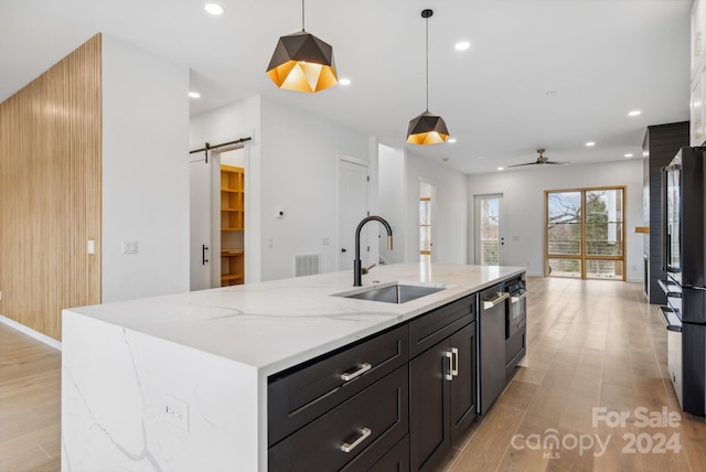 kitchen with sink, a barn door, light hardwood / wood-style floors, decorative light fixtures, and a kitchen island with sink