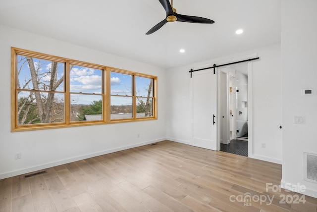 unfurnished bedroom with ceiling fan, a barn door, light hardwood / wood-style floors, and ensuite bath