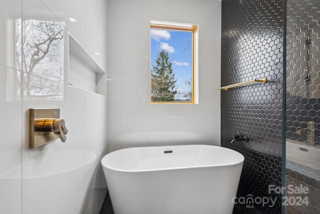 bathroom with a bathing tub, tile walls, and a healthy amount of sunlight