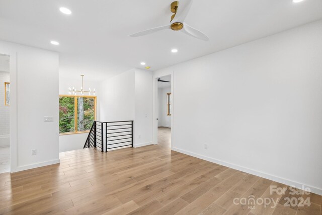 unfurnished room featuring ceiling fan with notable chandelier and light hardwood / wood-style floors