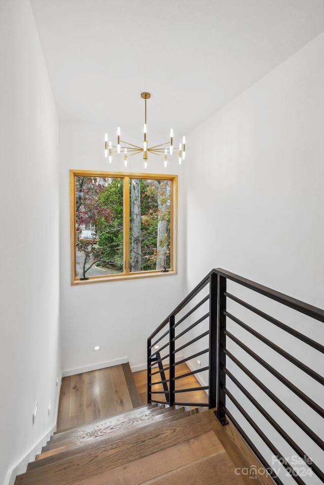 staircase featuring wood-type flooring and an inviting chandelier