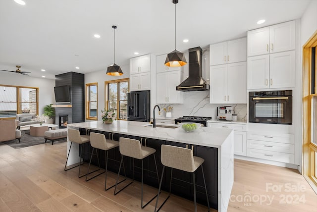 kitchen featuring sink, wall chimney exhaust hood, high end refrigerator, oven, and a center island with sink