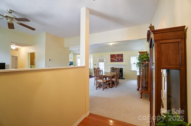 interior space featuring light carpet, baseboards, a ceiling fan, open floor plan, and a fireplace