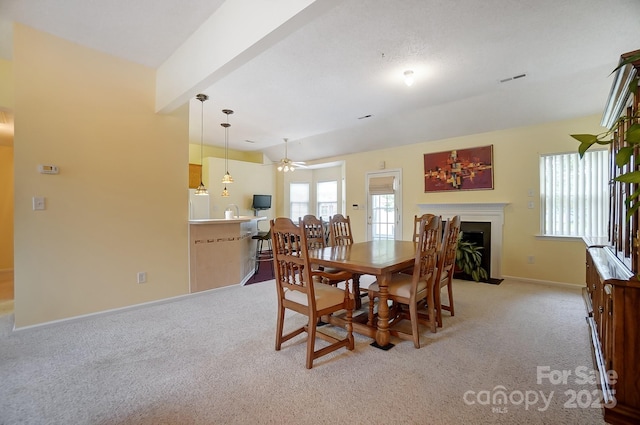 dining area with a healthy amount of sunlight, a fireplace with flush hearth, baseboards, and light colored carpet