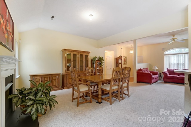 dining room featuring lofted ceiling, a fireplace, a ceiling fan, and light colored carpet