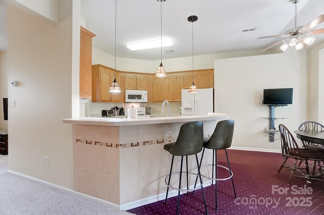 kitchen featuring dark colored carpet, light countertops, visible vents, white appliances, and a kitchen bar