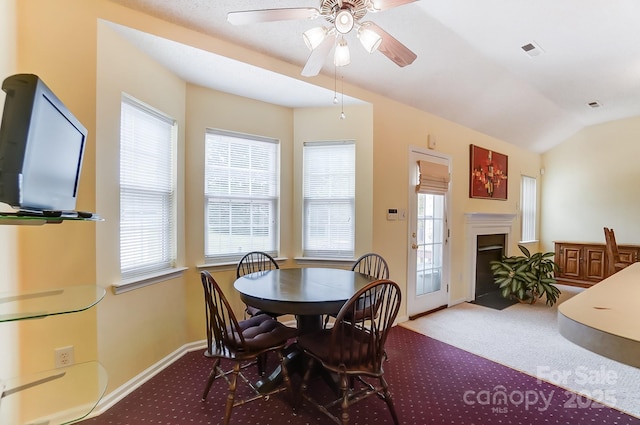 carpeted dining area with a fireplace with flush hearth, a healthy amount of sunlight, visible vents, and vaulted ceiling