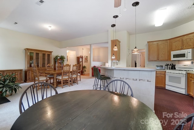 kitchen with dark colored carpet, visible vents, hanging light fixtures, a sink, and white appliances