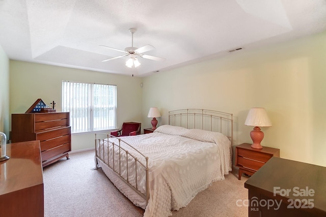 bedroom with a ceiling fan, a tray ceiling, visible vents, and light carpet