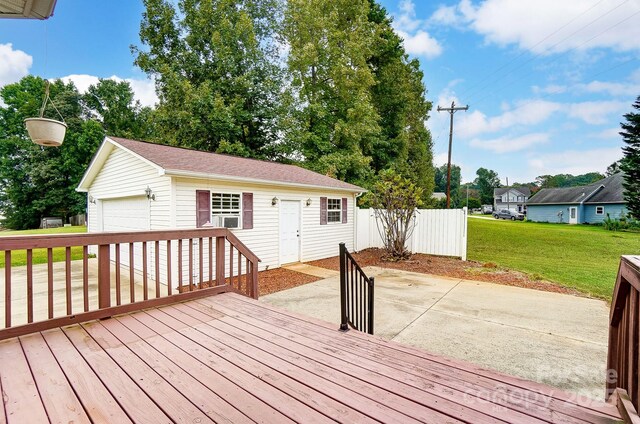 wooden deck featuring an outbuilding, a detached garage, a lawn, a patio area, and fence