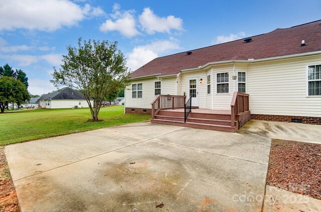 back of house with a deck, roof with shingles, crawl space, a lawn, and a patio area